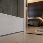 Habillage mur intérieur PVC blanc près d’une douche vitrée, effet bois au fond.
